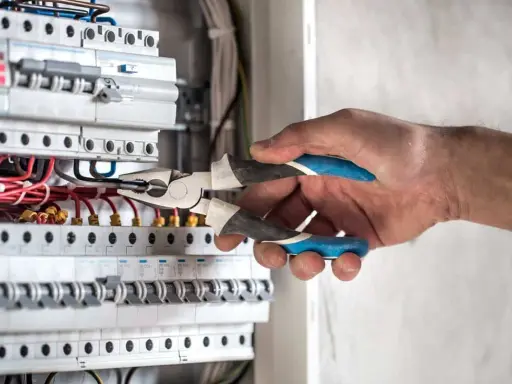 Elektryk pracuje przy skrzynce z bezpiecznikami. Gdy zgłosić brak prądu, warto sprawdzić właśnie takie instalacje.