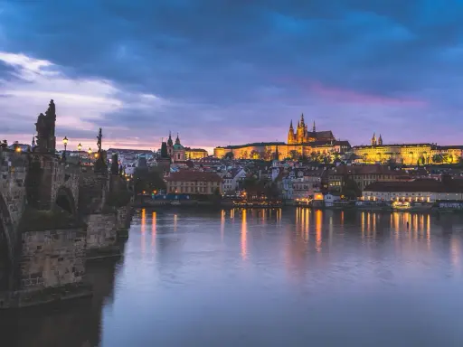 Nastrojowa fotografia nocna Pragi: Most Karola i Zamek na Hradczanach w blasku świateł, odbijających się w Wełtawie.