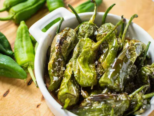 Friggitelli in padella, cotti e lucidi, cosparsi di sale grosso, in una ciotola bianca.