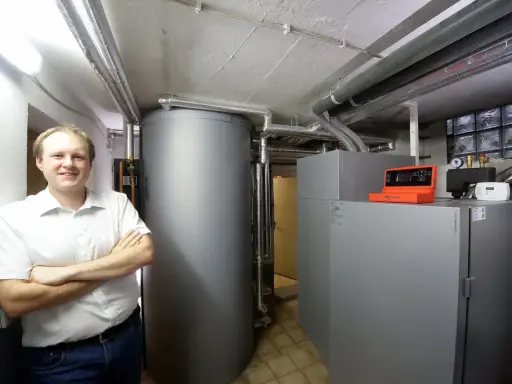 Mann vor Pelletheizung und großem Speicher in Heizungsraum.