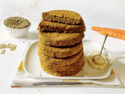 Impilati hamburger di lenticchie dorati, con lenticchie secche, carote e una salsa cremosa in un piatto.