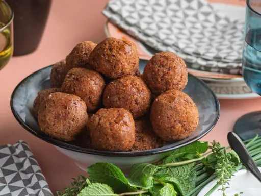 Un piatto colmo di polpette di fagioli dorate, guarnito con erbe fresche.