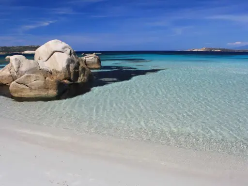 Spiaggia bianca e rocce granitiche sull'isola della Maddalena, con acque cristalline e un cielo azzurro intenso.