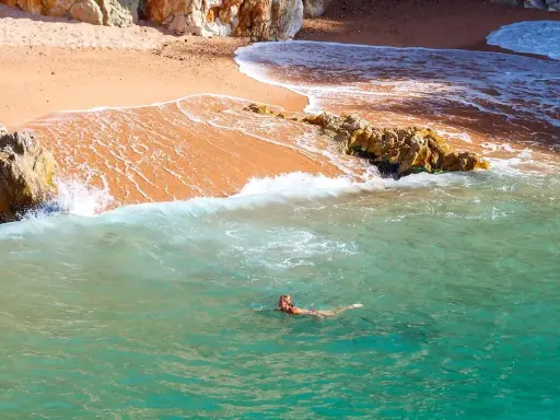 Eine Frau schwimmt im türkisfarbenen Meer vor einer sandigen Bucht in Palamós, Spanien.