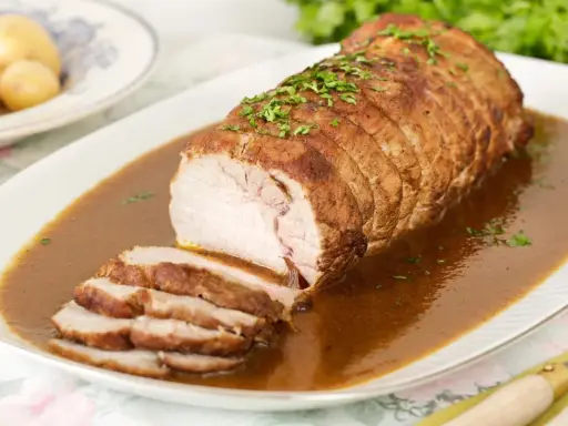 Lomo de cerdo al horno en papel aluminio, jugoso y tierno, bañado en salsa y espolvoreado con perejil.