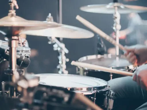 Gros plan sur un set de batterie, avec des baguettes en action. Différents types de tambour et cymbales sont visibles.