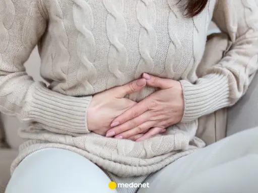 Kobieta trzyma się za brzuch, odczuwając ból brzucha po jedzeniu.