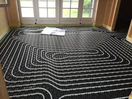 Instalación suelo radiante con tuberías blancas sobre paneles negros. Un plano yace sobre el suelo.