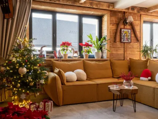 Przytulny salon z choinką i prezentami, tworzący atmosferę **świąt w górach**. Drewniane ściany i okna dodają uroku.