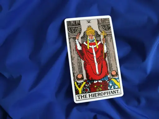 Karta Tarota "The Hierophant" na niebieskim tle. Postać w czerwonych szatach z tiarą i krzyżem.