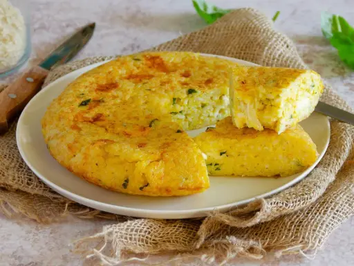 Una gustosa frittata di riso dorata, con erbe aromatiche, servita su un piatto bianco con una fetta tagliata.