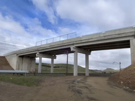 Un puente de hormigón cruza vías de tren. Los pilares de soporte, que son un estribo, sostienen la estructura. El cielo está nublado.