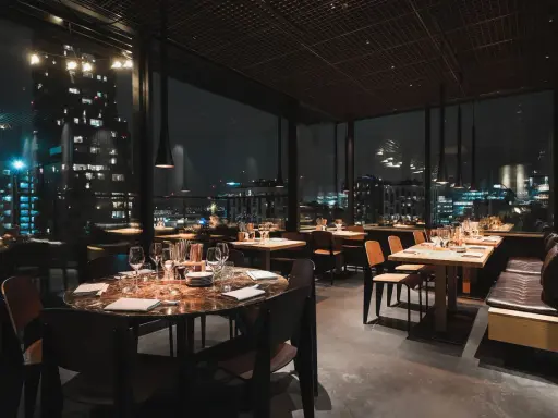 En mysig restaurang i Stockholm med vacker utsikt över stadens ljus på natten. Eleganta bord med dukning och bekväma sittplatser.