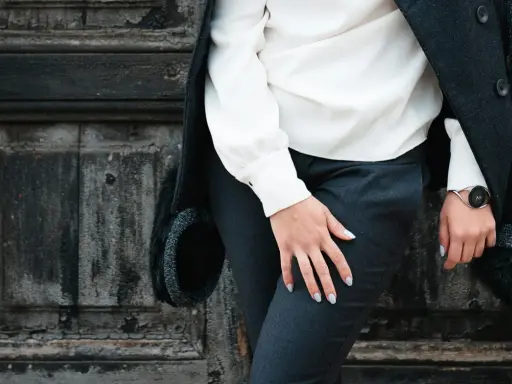 Elegancki facet w sukience, w białej bluzce i czarnych spodniach, stoi przy zniszczonych drzwiach.