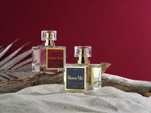 Dwa flakony perfum z etykietami "Dubai Elixir" i "Mamma Mia!", zawierające feromony damskie, stoją na piasku obok kawałka drewna.