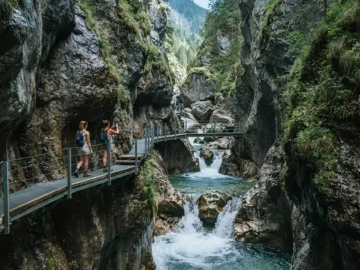 Due escursioniste attraversano passerelle metalliche nel suggestivo orrido di Uriezzo, con un fiume impetuoso che scorre tra le rocce.