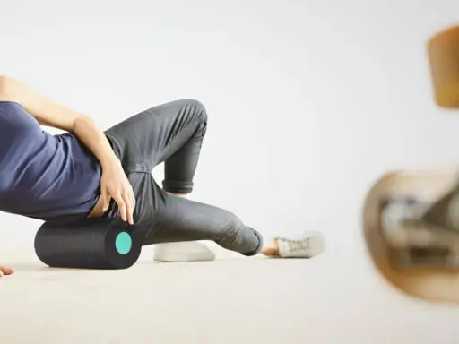 Frau rollt mit einer Faszienrolle über ihr Knie, um Muskelverspannungen zu lösen. Ein Skateboard ist im Vordergrund unscharf zu sehen.