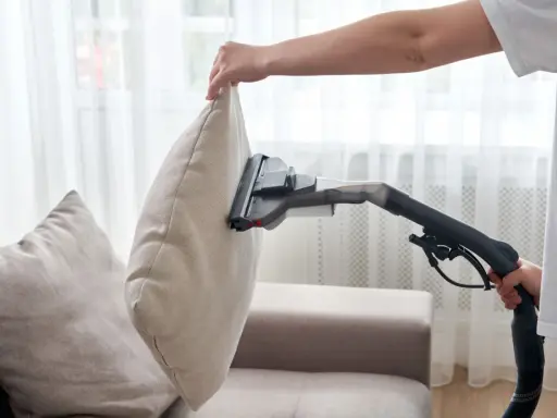En person dammsuger soffa och kuddar för att få bort damm och smuts.