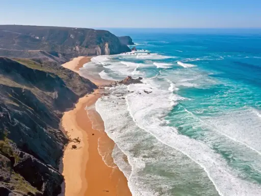 Atemberaubende Küstenlandschaft im Distrikt Faro, Portugal. Steile Klippen treffen auf einen goldenen Sandstrand und das türkisfarbene Meer mit tosenden Wellen.