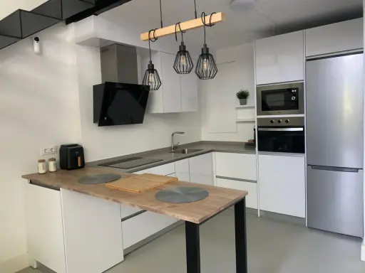 Cocina moderna con isla, electrodomésticos integrados y lámparas colgantes. Ideas para como diseñar una cocina funcional y elegante.