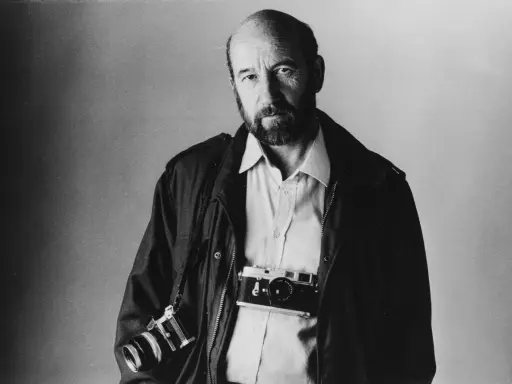 Ritratto di Gianni Berengo Gardin, fotografo con due macchine fotografiche al collo, sguardo intenso.