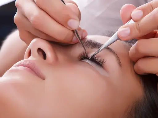 Pose de cils : quelle pince à épiler choisir pour un résultat parfait. Une esthéticienne applique des extensions de cils avec précision.