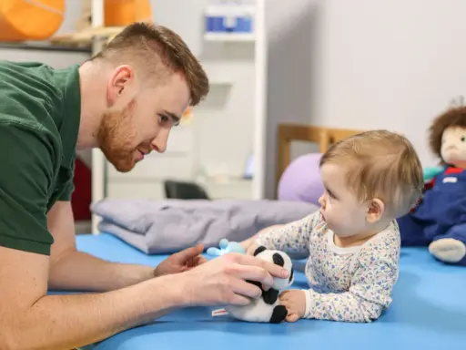 Osteopata dla dzieci delikatnie bawi się z niemowlęciem pluszową pandą, wspierając jego rozwój.