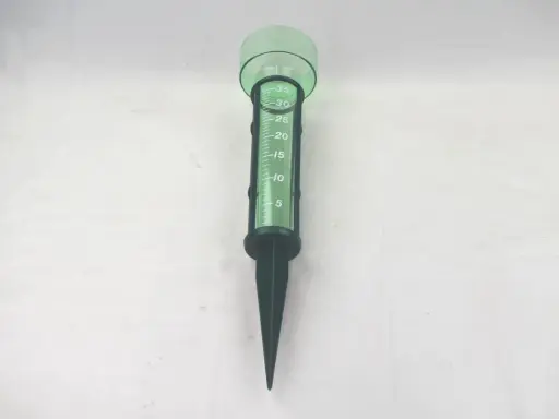 Pluviomètre vert avec graduations pour savoir comment lire un pluviomètre. Il est planté dans le sol.