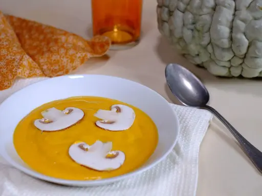 Soupe de courge orange avec des champignons, une serviette orange et une courge entière, évoquant une ambiance de Marina di Chioggia.