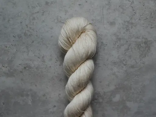 En härva av ljusbeige garn, troligen tencel, ligger på en grå, stenig bakgrund. Garnet är mjukt tvinnat och ger ett intryck av en tencel blow.