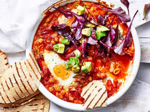 Herzhaftes Gericht mit pochierten Eiern in Tomatensoße, Bohnen, Avocado und Rotkohl. Perfekt für gesunde Rezepte Abendessen. Dazu geröstetes Fladenbrot.
