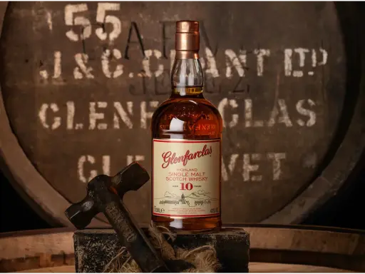 Butelka Glenfarclas 10 Year Old, jedna z 10 najlepszych whisky, na tle beczki. Młotek sugeruje rzemiosło.