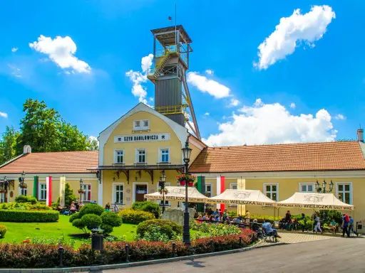 Wieliczka atrakcje: Szyb Daniłowicza, żółte budynki kopalni, zielony ogród i ludzie odpoczywający pod namiotami.