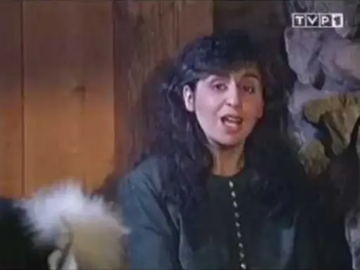 Kobieta z ciemnymi włosami, w zielonej bluzce, mówi do kamery. Chciałabym być tam gdzie ty, w tym przytulnym wnętrzu.