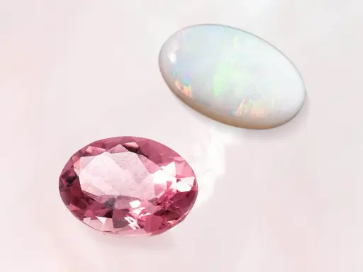 Due gemme ovali, una rosa e un opale, brillano su sfondo chiaro. La pietra rosa ricorda la pietra d'ottobre.