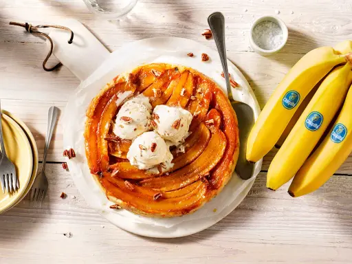 Tarte banane caramel beurre salé, garnie de boules de glace à la vanille et de noix de pécan. Des bananes Chiquita sont à côté.