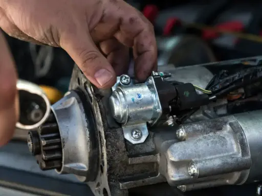 Mechanik naprawia rozrusznik w aucie, przykręcając element.