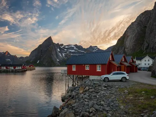 Röda fiskestugor vid vattnet i Lofoten, perfekt boende för en stuga-semester med dramatiska berg i bakgrunden.