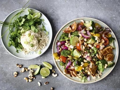 Två tallrikar med mat till många: en med ris, koriander och lime, den andra med kyckling, grönsaker och cashewnötter.