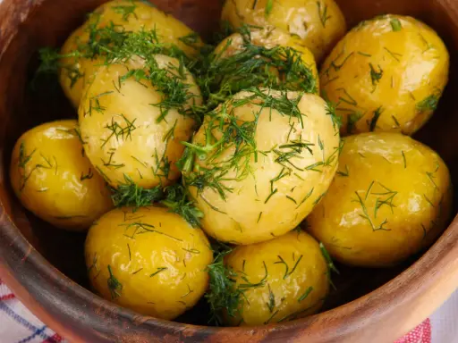 Ziemniaki gotowane w drewnianej misce, posypane świeżym koperkiem. Aromatyczne i apetyczne danie.
