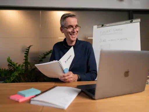 Lehrer erklärt **adjektive und adverbien englisch** mit einem Flipchart und Notizbuch.
