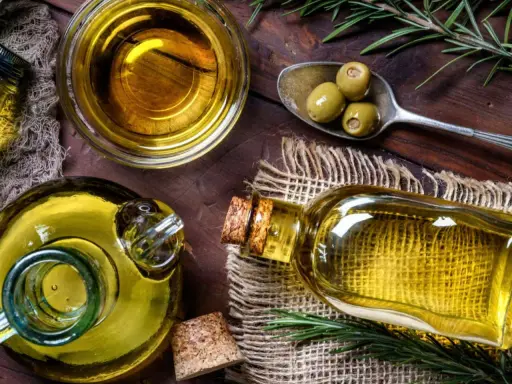 Aceite de oliva en botellas y cuenco, con aceitunas y romero. A pesar de sus beneficios, hay desventajas del aceite de oliva, como su precio.