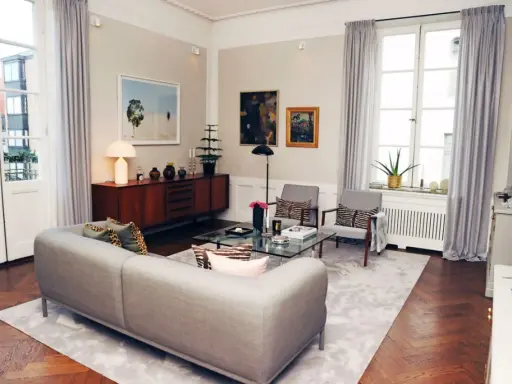 Ett modernt vardagsrum med en grå soffa, glasbord och konst. Johan Pråmell skulle trivas här.