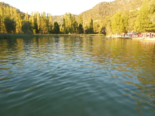 Gente disfrutando del agua en la playa de Cañamares, rodeada de árboles y montañas.
