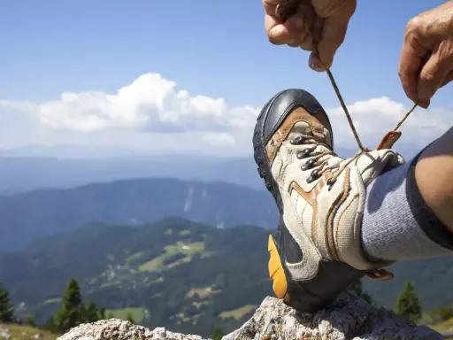 Ręka zawiązuje sznurówki buta trekkingowego na tle górskiego krajobrazu. Właściwe wiązanie butów to klucz do komfortowej wędrówki.