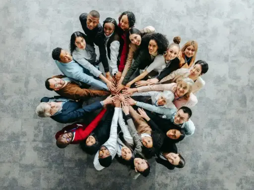 Grupa ludzi w kręgu, dłonie złożone na środku, symbolizująca współpracę przy wypełnianiu kwestionariusza osobowego dla osoby ubiegającej się o zatrudnienie.