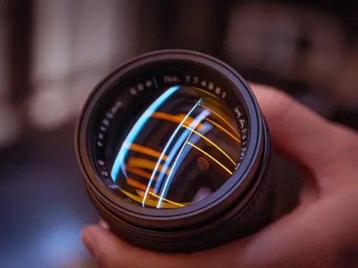Primer plano de un objetivo fotográfico con reflejos de luces azules y naranjas.