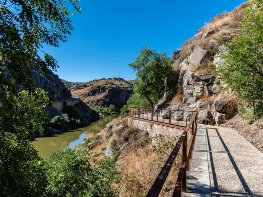 Sendero con barandilla de metal junto a un río y rocas, ideal para rutas senderismo Toledo.
