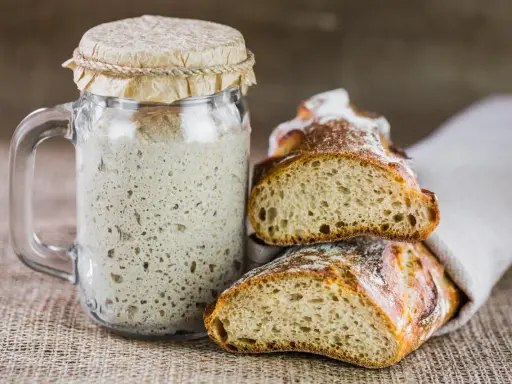 Un bocal de levain actif, prêt à être utilisé pour entretenir son levain, à côté de deux belles tranches de pain artisanal.
