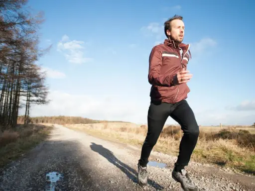 Mann joggt bei 10 Grad in einer leichten Jacke und Hose auf einem Feldweg.